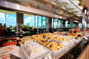 A buffet with various food items, including pastries and salads, in a well-lit room with large windows.
