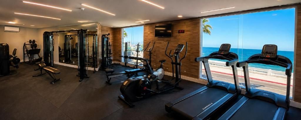 A gym with treadmills, ellipticals, and weight machines, overlooking a beach.