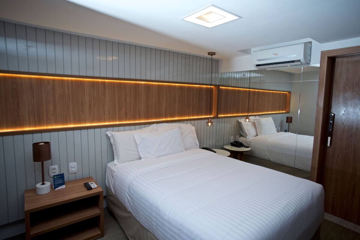 Ein modernes Hotelzimmer mit einem großen Bett, Nachttischen, einem Spiegel und einer Klimaanlage.