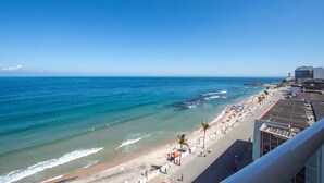 Een strand met helderblauw water, een zandstrand en een promenade met palmbomen.
