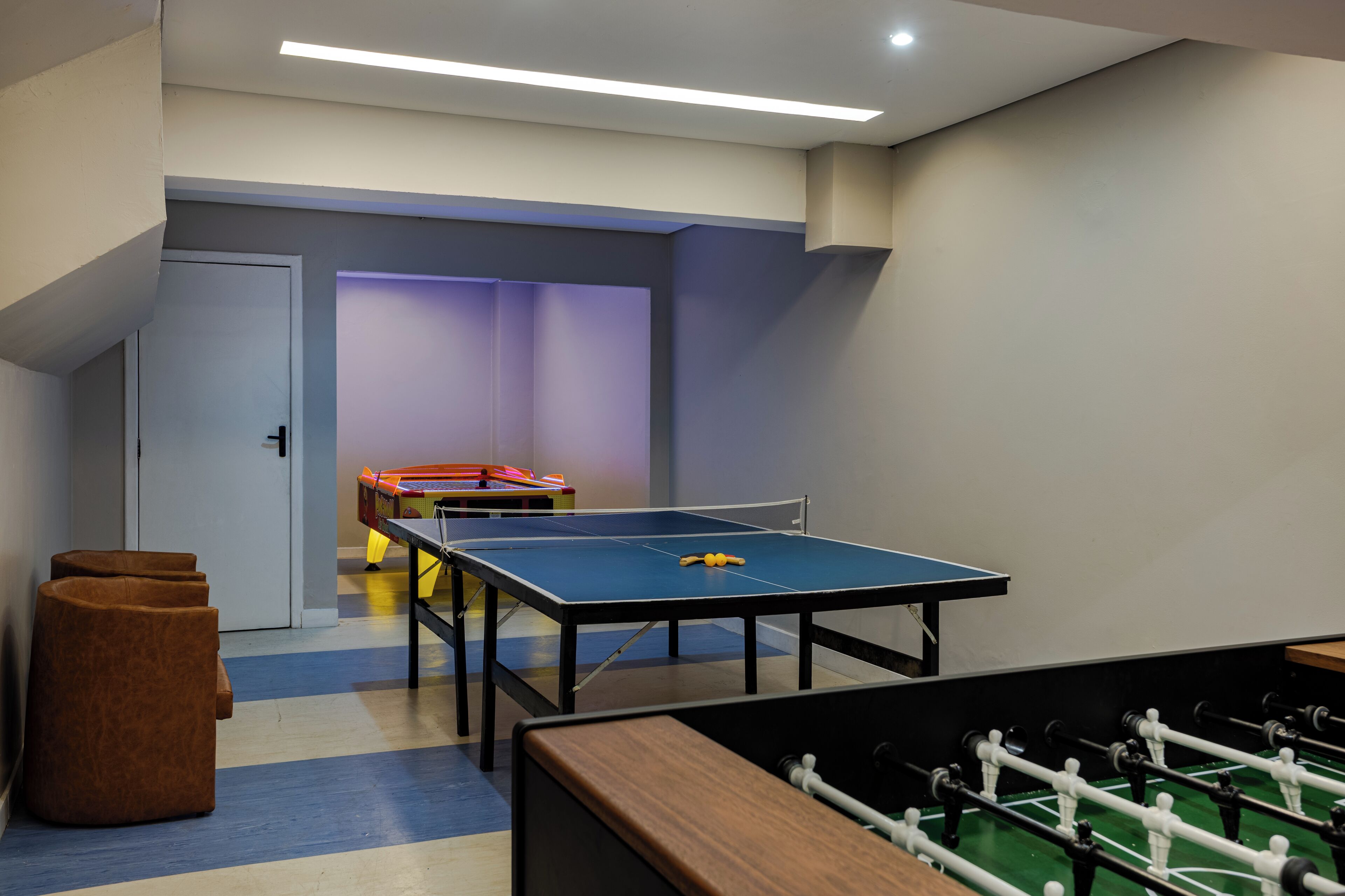A room with a ping pong table, a foosball table, and a door.