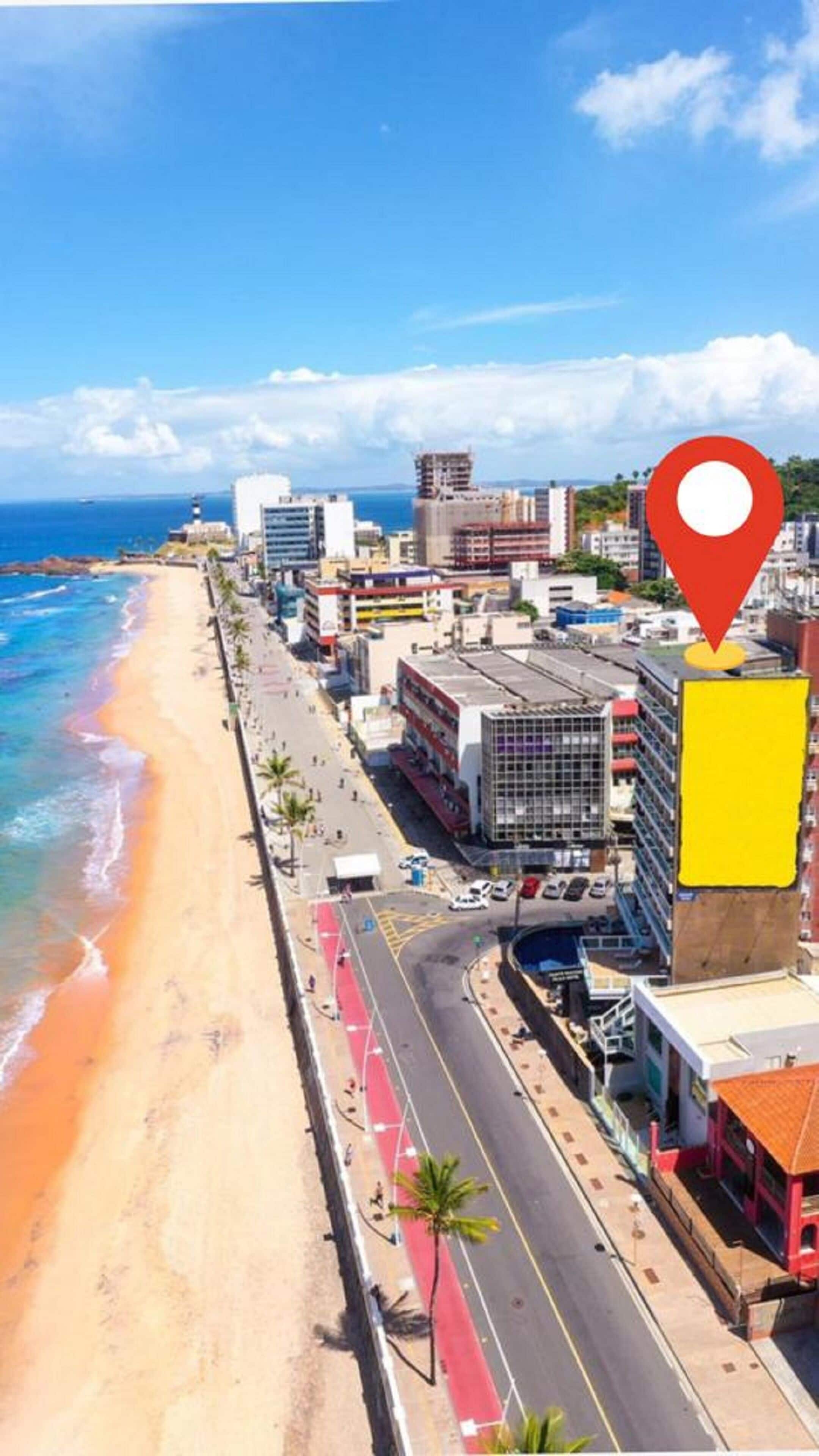 A coastal cityscape with a beach, buildings, and a road with red lanes.