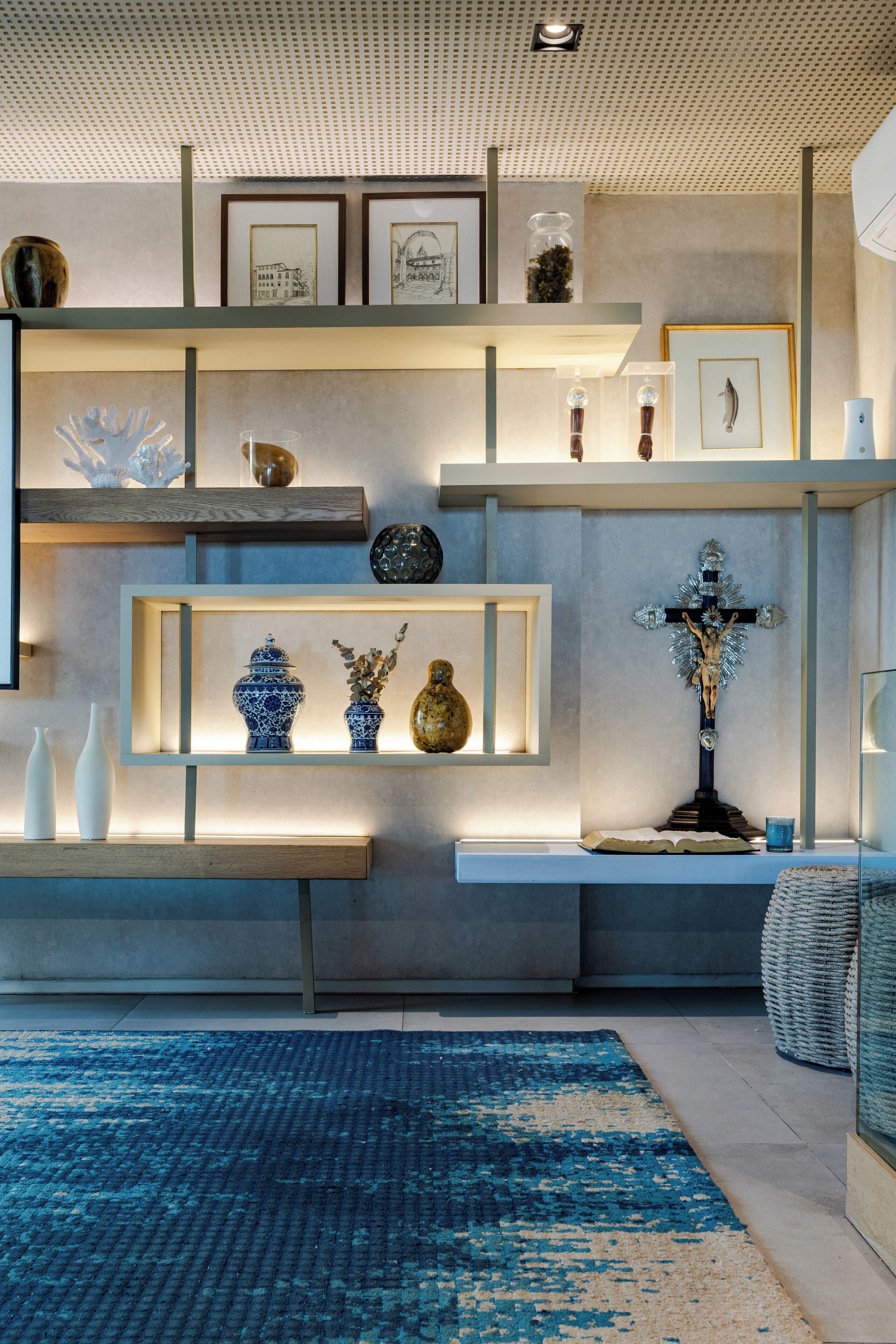 Een modern interieur met een blauw patatoffel, planken met decoratieve objecten, en een kruis.