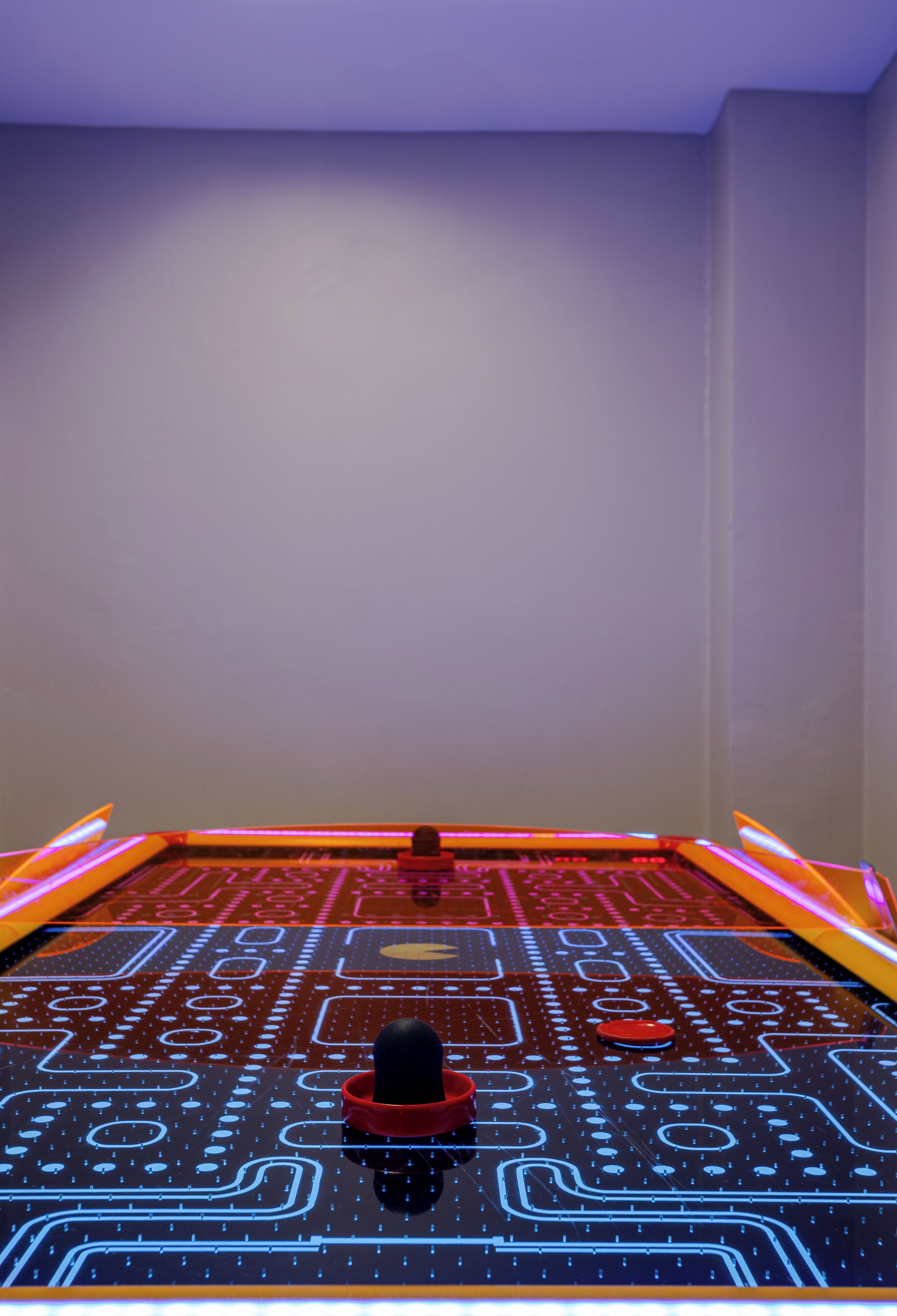 A room with a large, illuminated circuit board design on the floor, a red object in the center, and a plain wall.