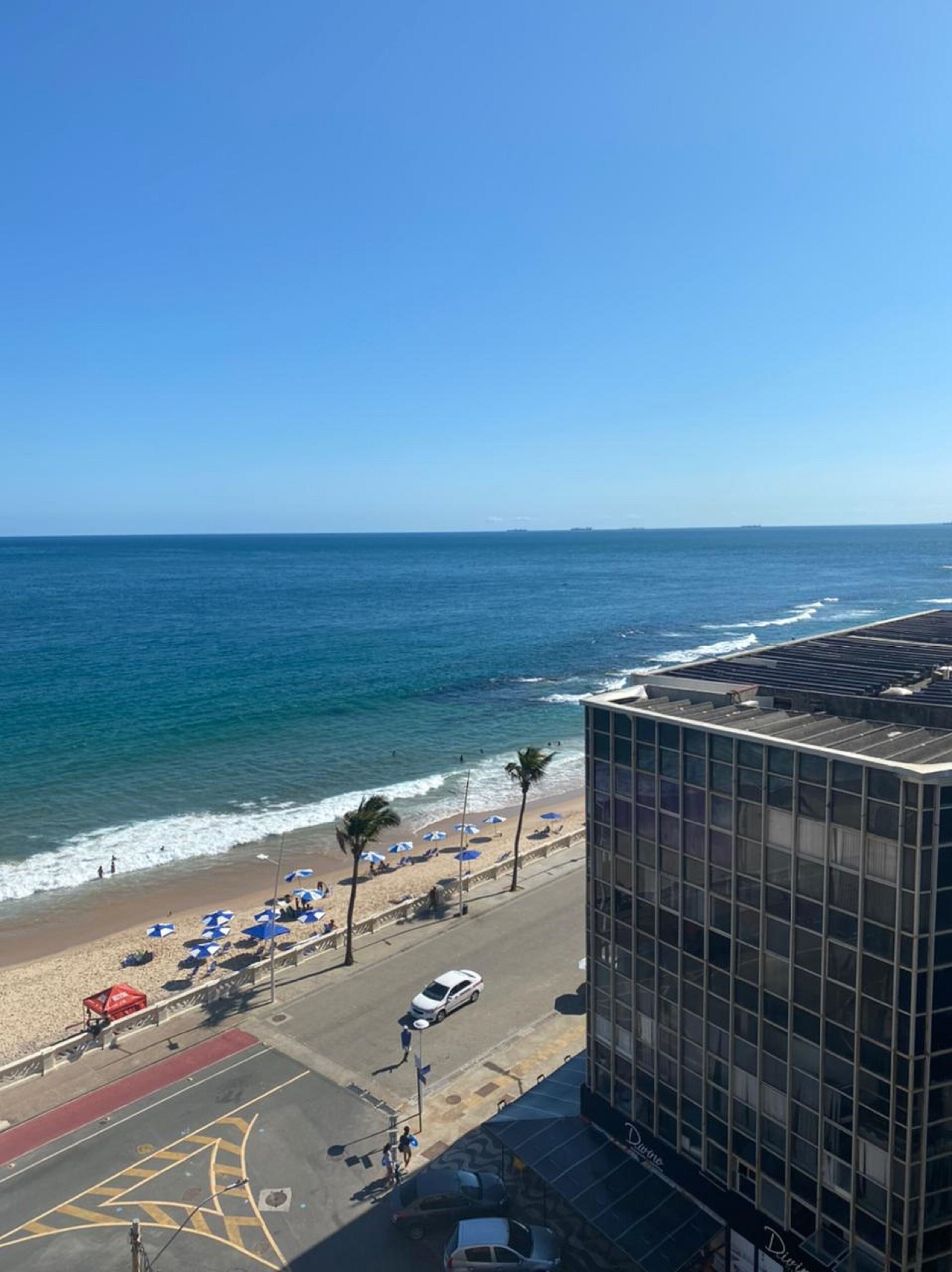 Paesaggio costiero con spiaggia, ombrelloni e un edificio con facciata in vetro.