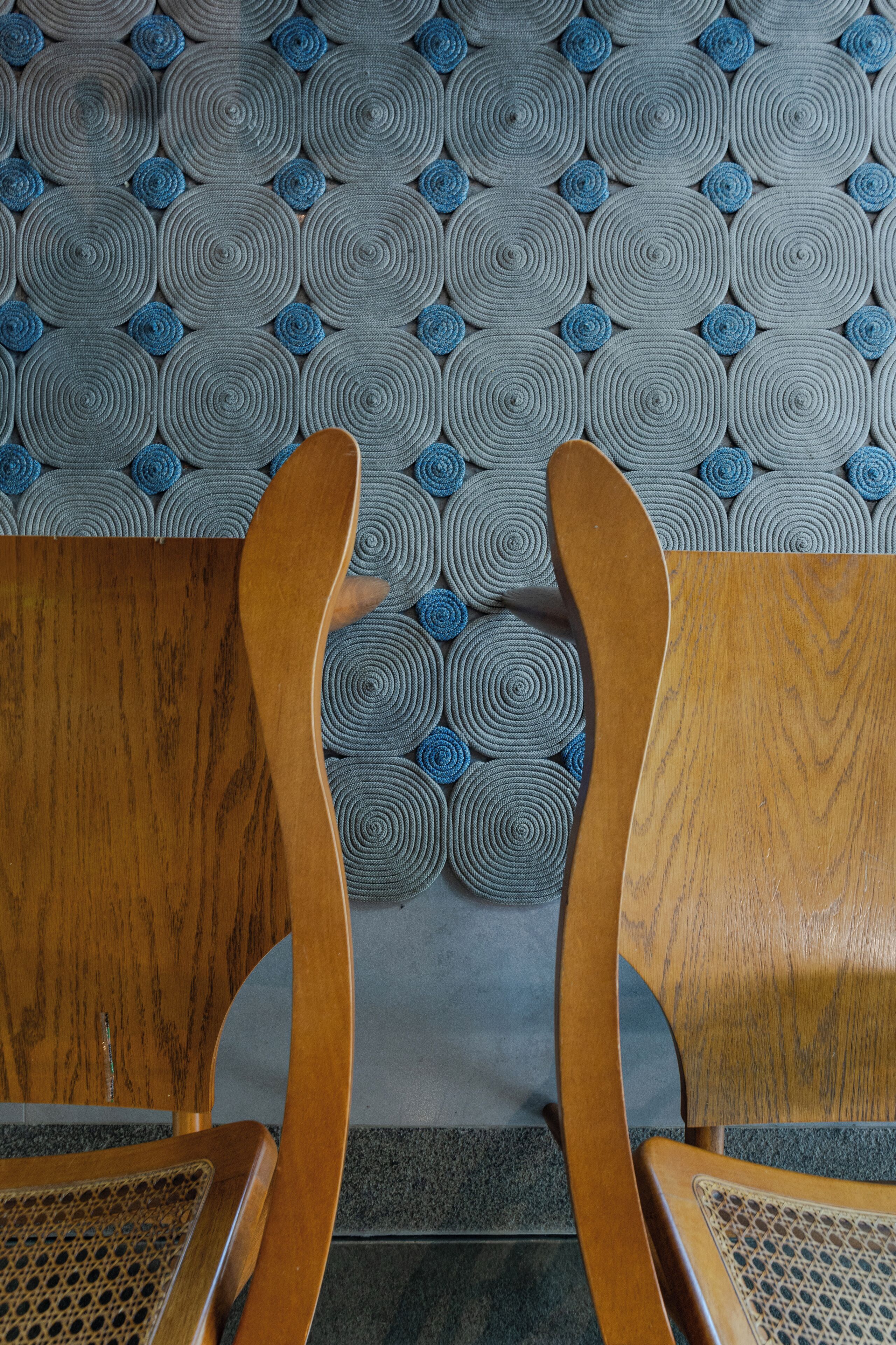 Two wooden chairs with woven seats and backs, positioned in front of a wall with a circular pattern.