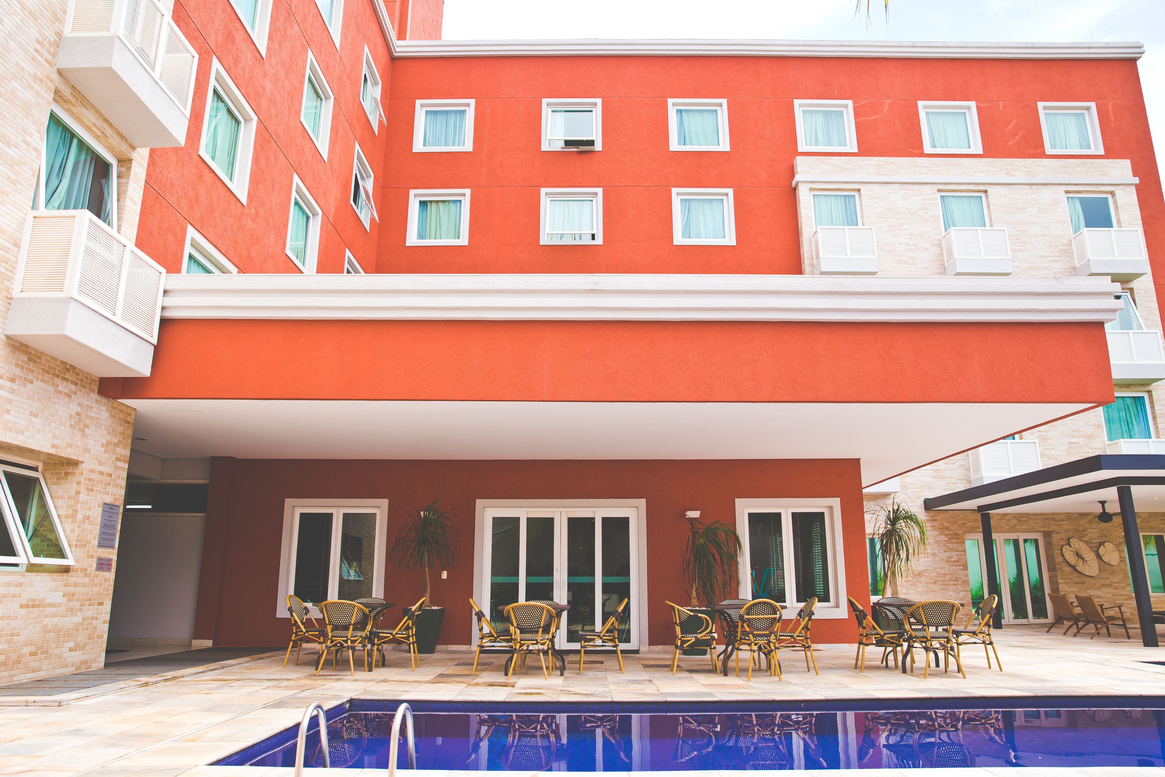 A red building with multiple balconies, a pool area with outdoor furniture, and a covered patio.