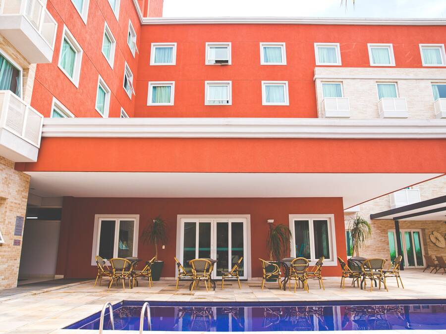 Un bâtiment rouge doté de nombreux balcons, un espace piscine avec des meubles d’extérieur et une terrasse couverte.