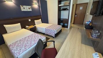 Ein Hotelzimmer mit zwei Betten, einem Schreibtisch, einem Stuhl, einem Kleiderschrank und einem Spiegel.