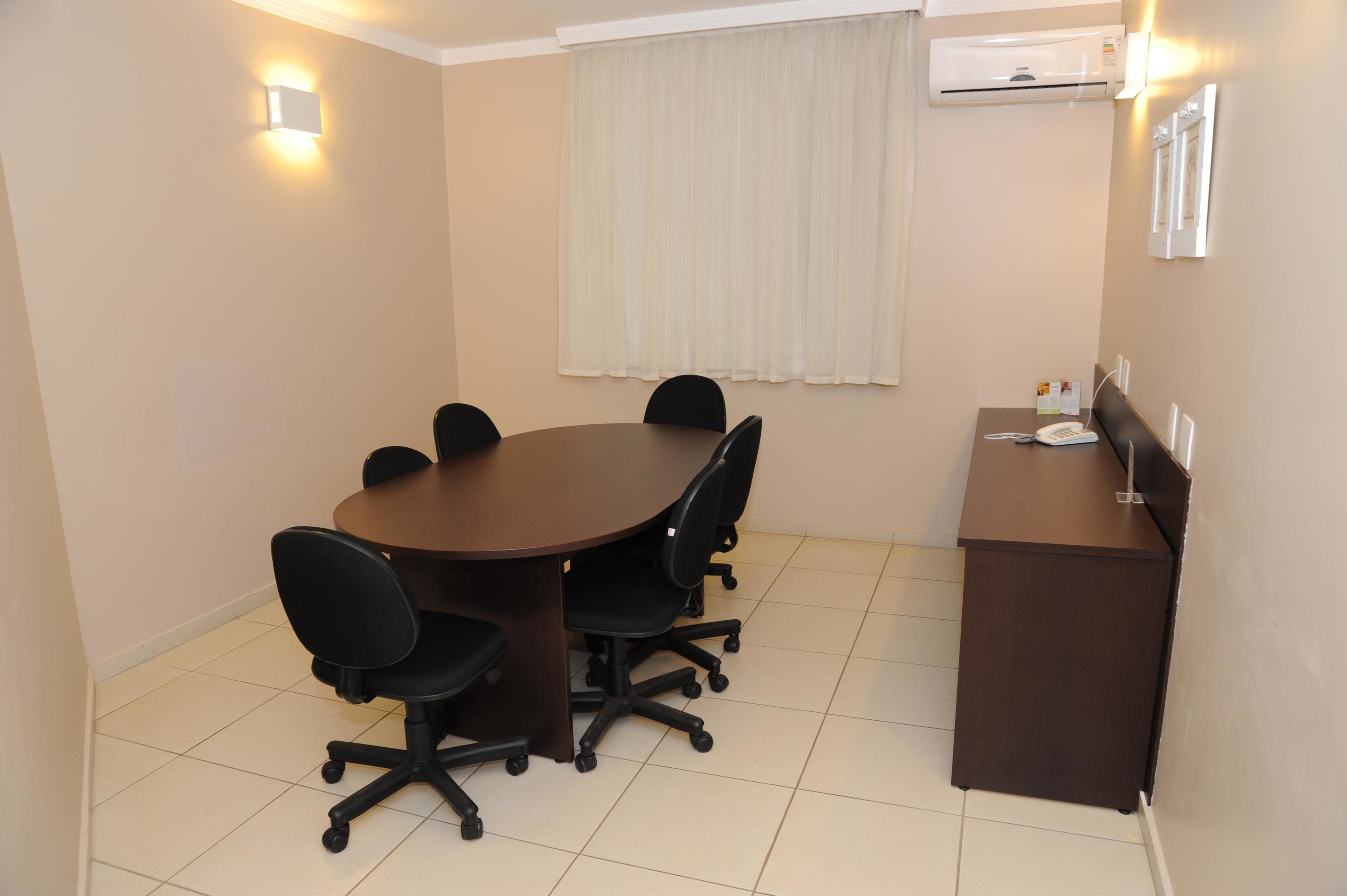 A conference room with a round table, six black office chairs, a brown desk, and a white air conditioning unit on the wall.