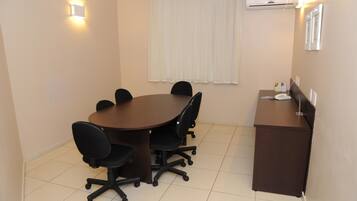 A conference room with a round table, six black office chairs, a brown desk, and a white air conditioning unit on the wall.