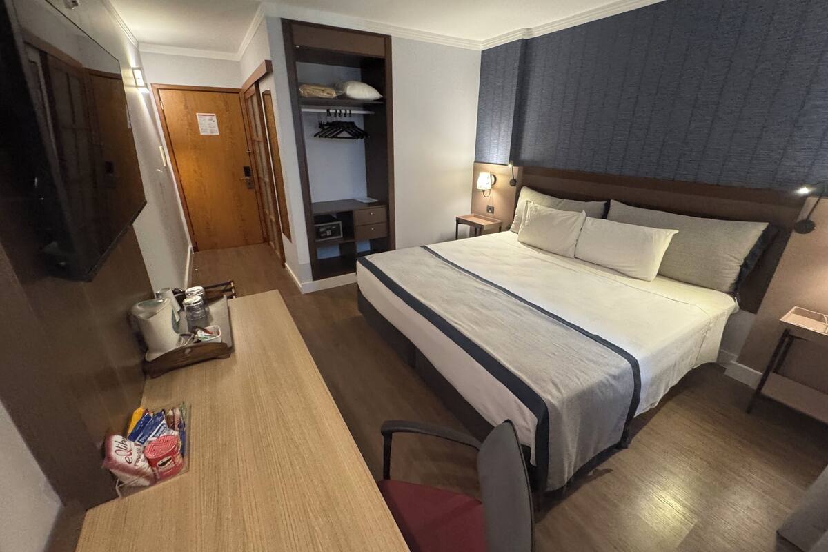 A hotel room with a bed, bedside table, chair, desk, and a wardrobe.