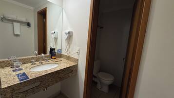 Un baño con encimera de granito, dos lavamanos, un espejo, toallero, secador de pelo y retrete.