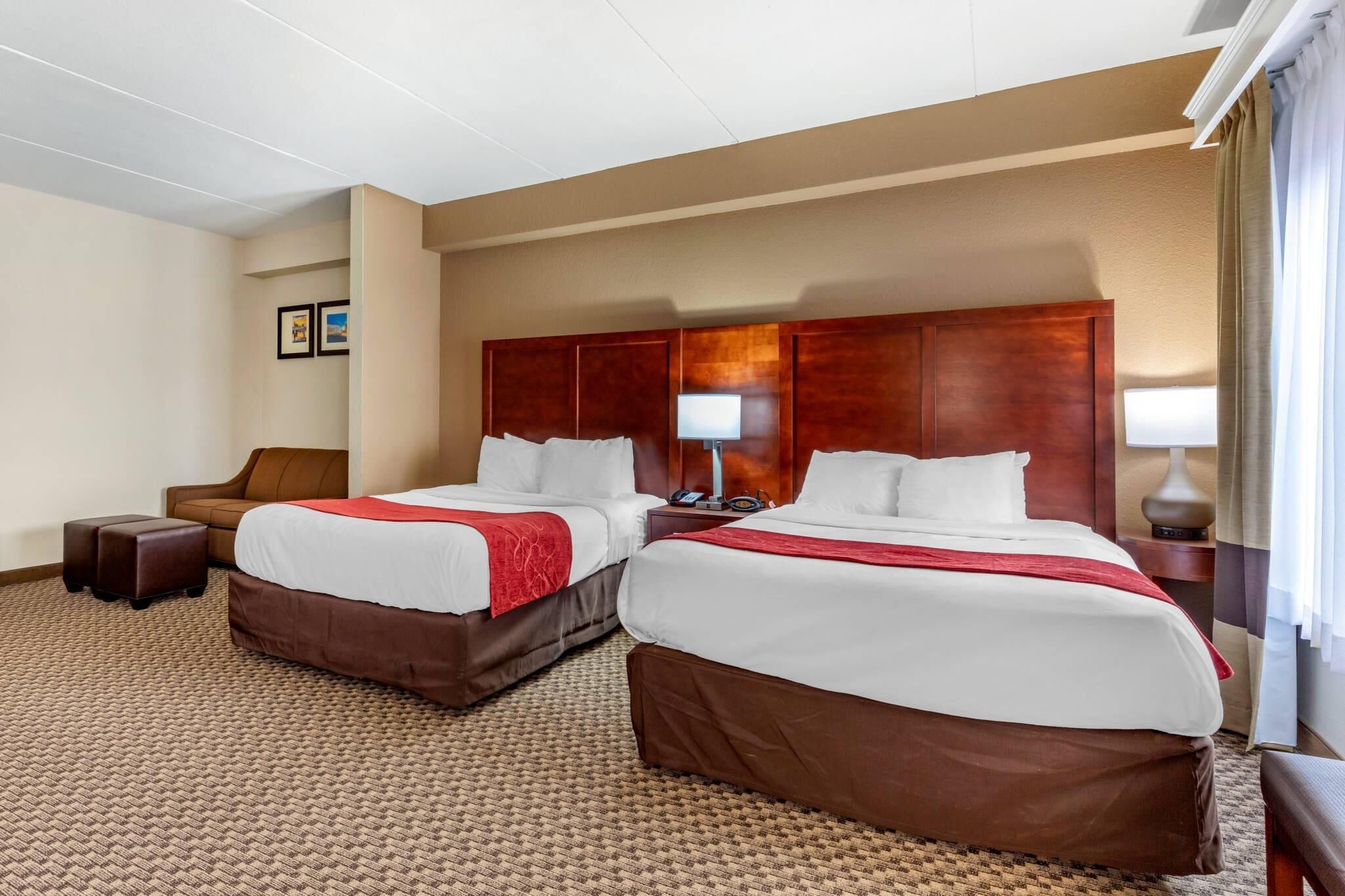 Una habitación de hotel con dos camas, un sillón de cuero marrón, una mesita y una lámpara.