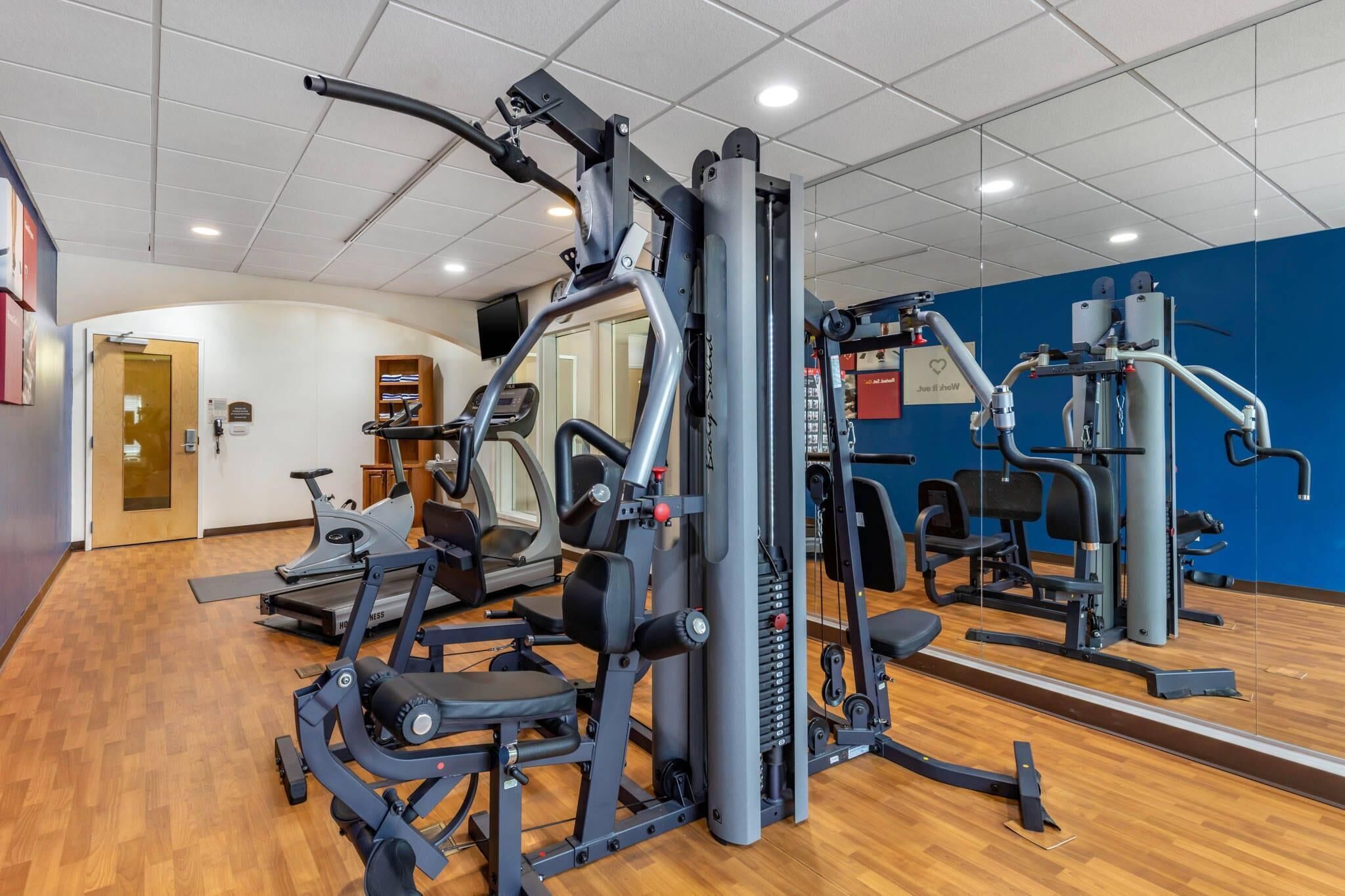 Un gimnasio con máquinas de cardio, equipo de levantamiento de pesas y un espejo grande.