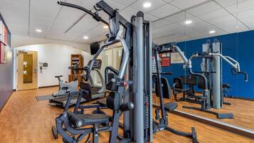 Un gimnasio con máquinas de cardio, equipo de levantamiento de pesas y un espejo grande.