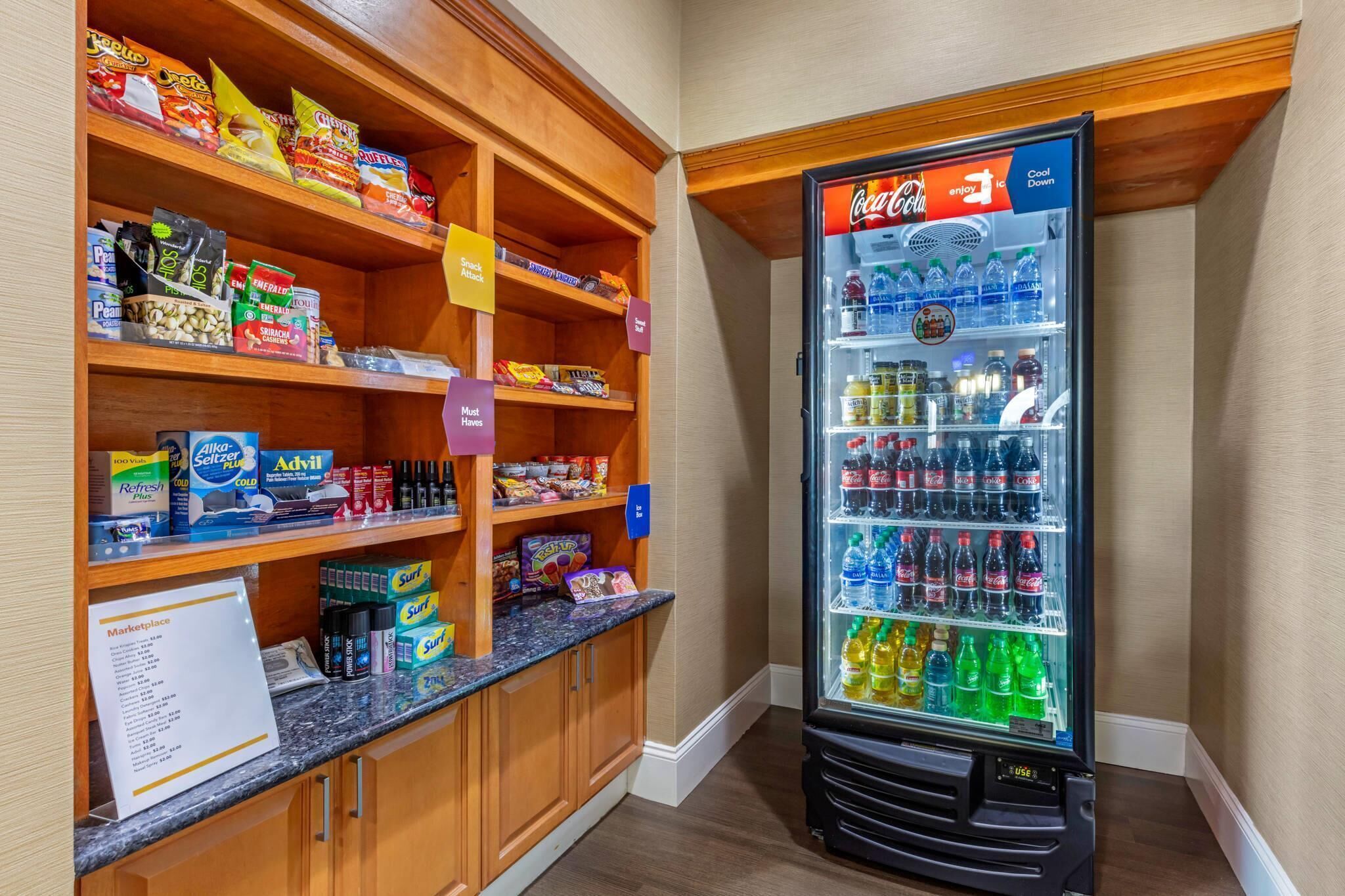 A vending machine stocked with various beverages and snacks, adjacent to a wooden shelf unit with packaged goods.