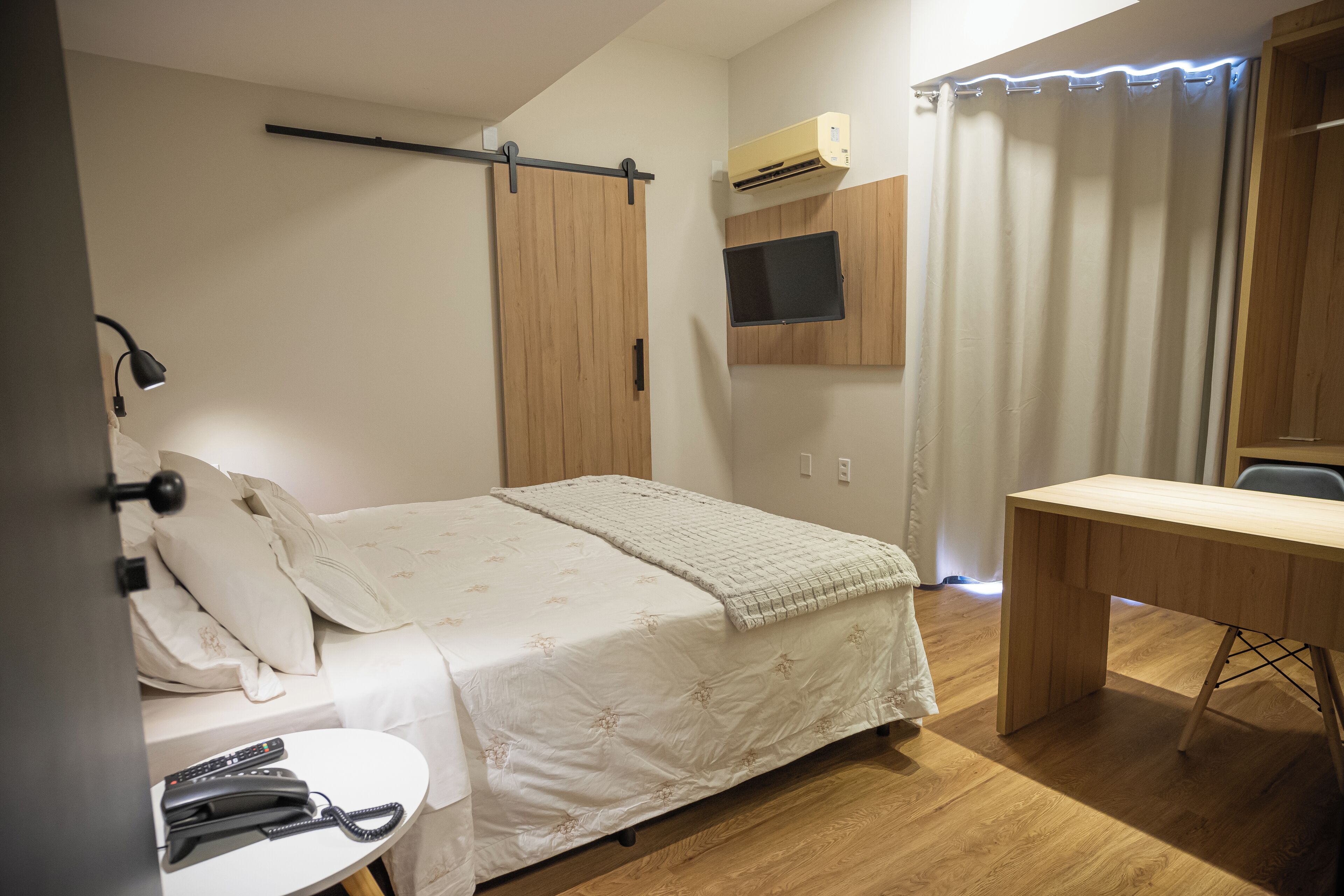 Un dormitorio con cama, mesita de noche, escritorio y televisor montado.