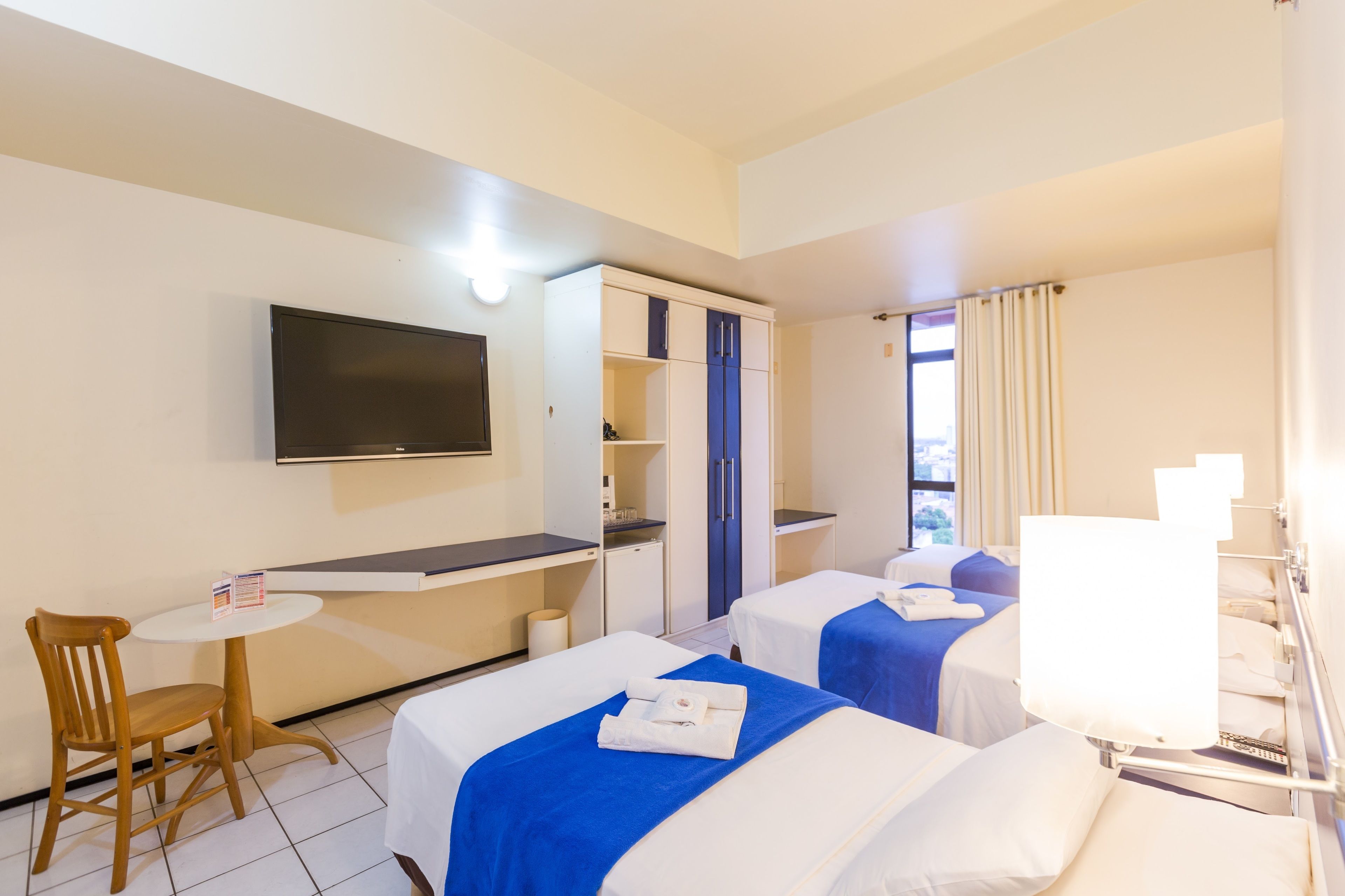 Habitación de hotel con dos camas, un escritorio, una silla, un televisor y una ventana con cortinas.