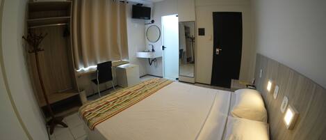 A hotel room with a bed, a desk, a chair, a wardrobe, a mirror, a television, and a bathroom.