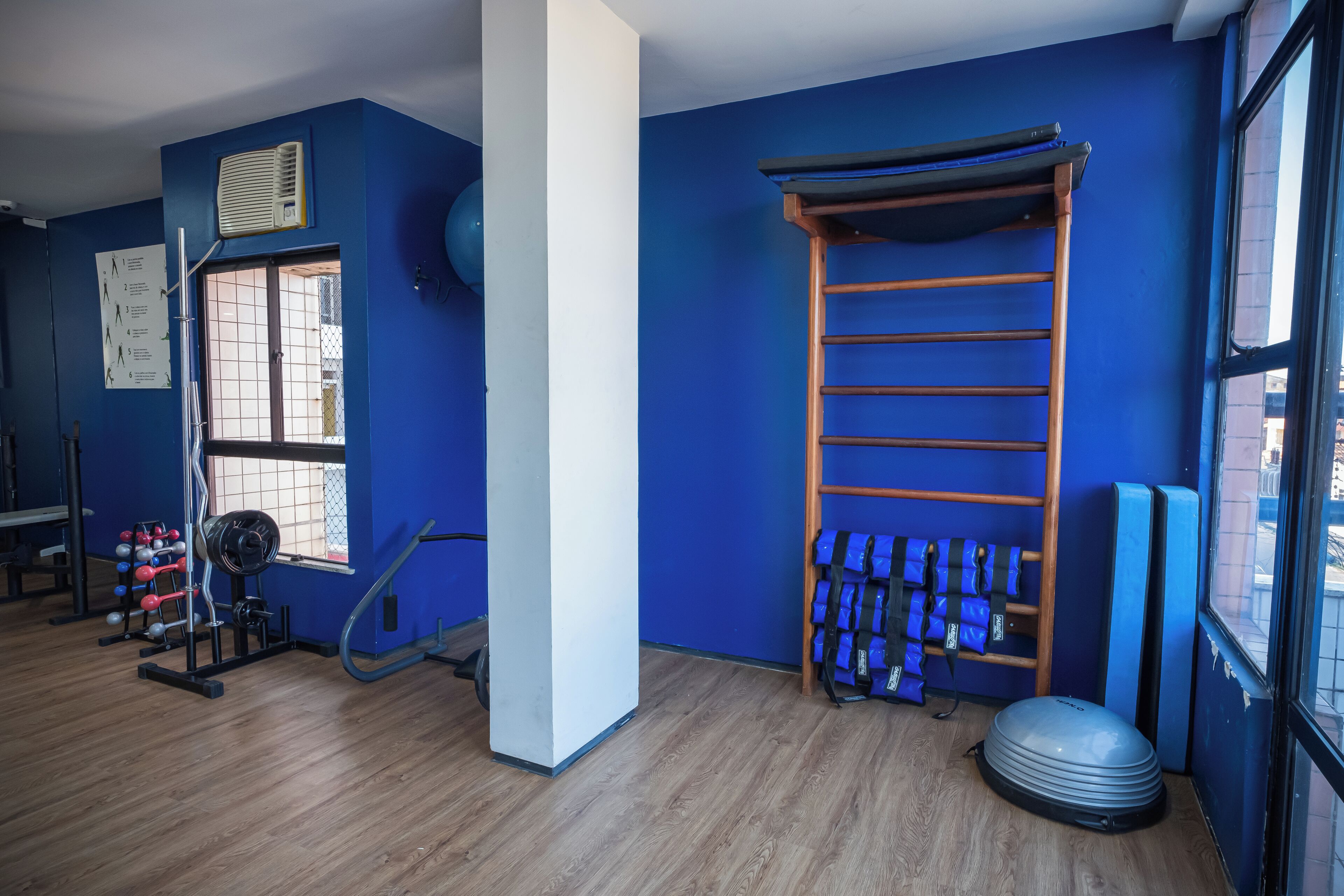 A gym with blue walls, a wooden floor, a weight rack, a pull-up bar, and a yoga mat.