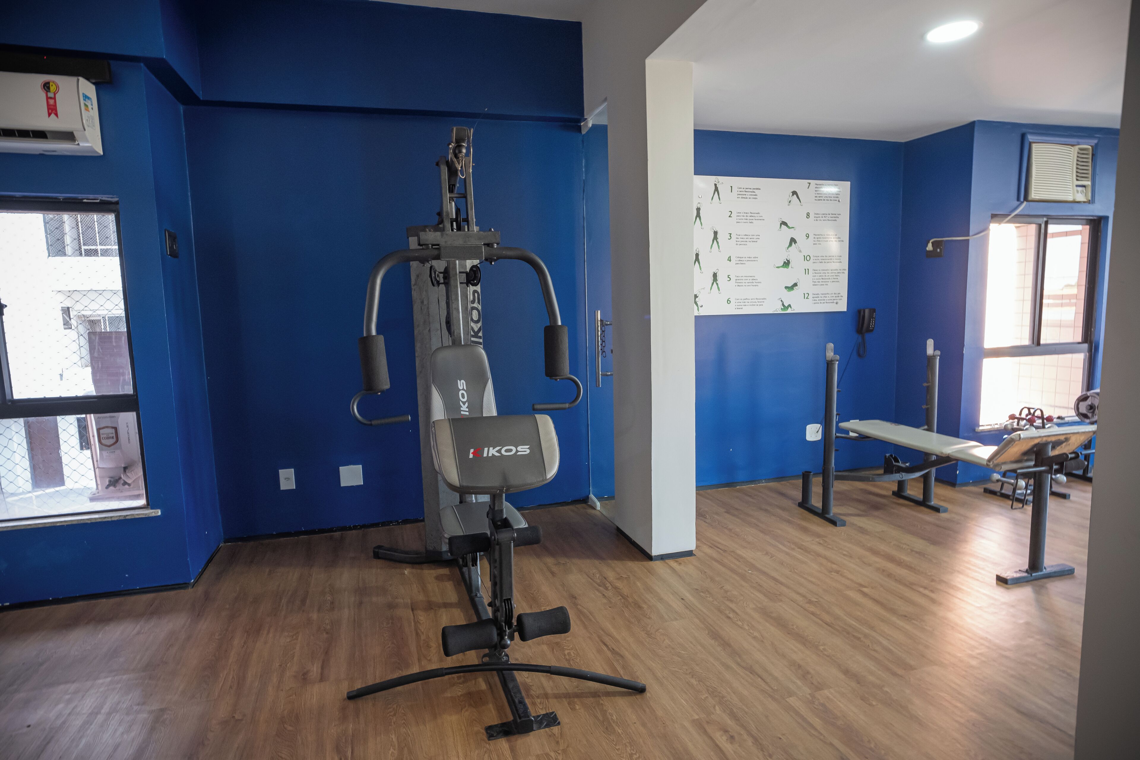 A gym with blue walls, a weight bench, and a KIOS fitness machine.