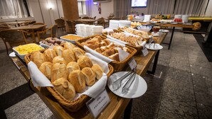 Un buffet con diversi tipi di pane e dolci, un cartello che indica 'Pao Frances' e una sala da pranzo con tavoli e sedie.