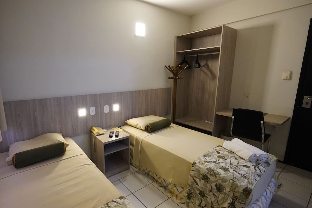 Una habitación de hotel con dos camas, un escritorio, un armario y un espejo.