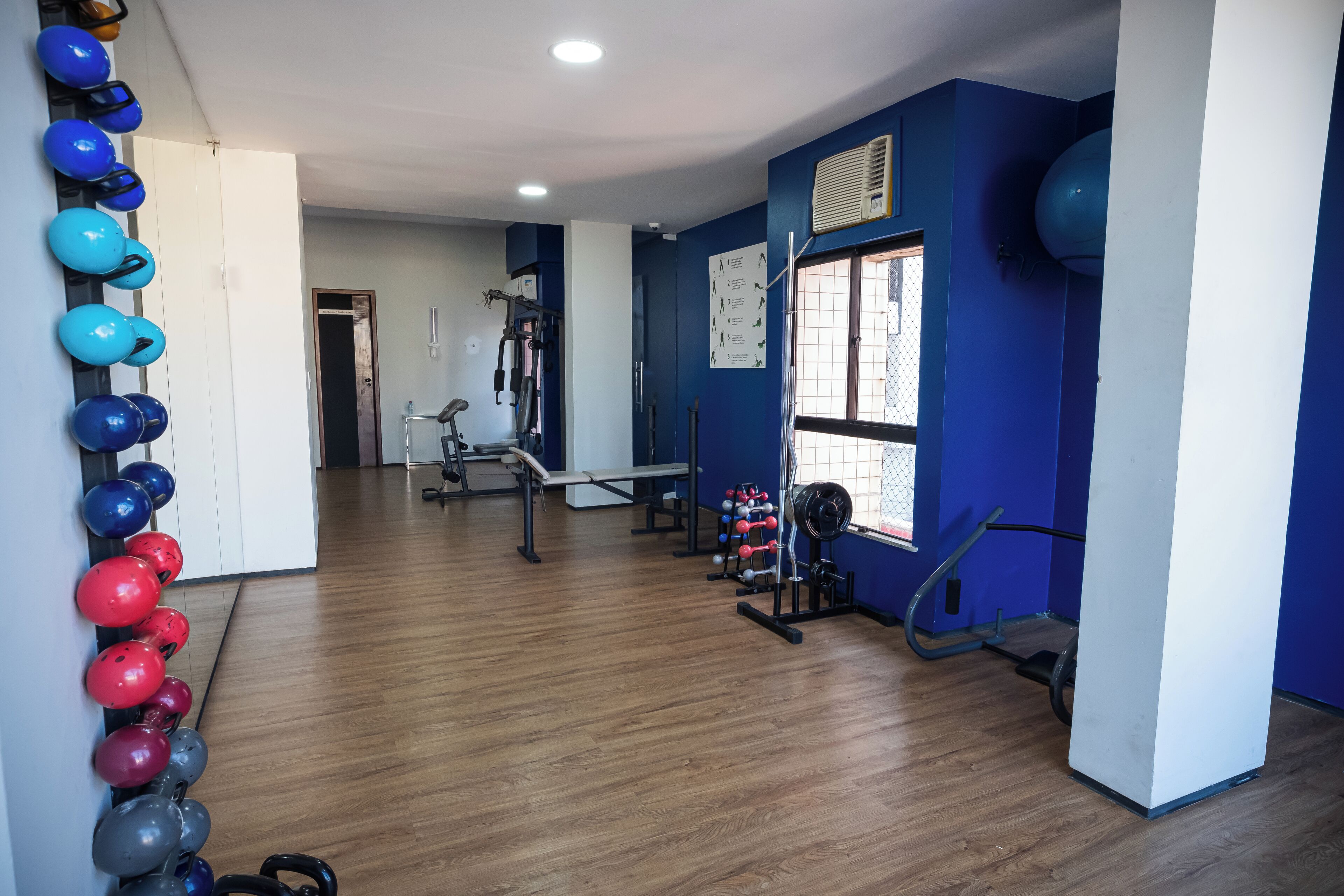 Un gimnasio con diverso equipo de ejercicio, un estante con cascos montado en la pared y un ventanal que proporciona luz natural.