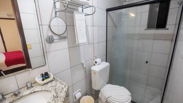 A bathroom with a granite sink, a toilet, a glass-enclosed shower, and a towel rack with folded towels.