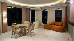 Un interno moderno con un tavolo rotondo e sedie, un divano e ampie finestre ad arco che si affacciano sulla città.