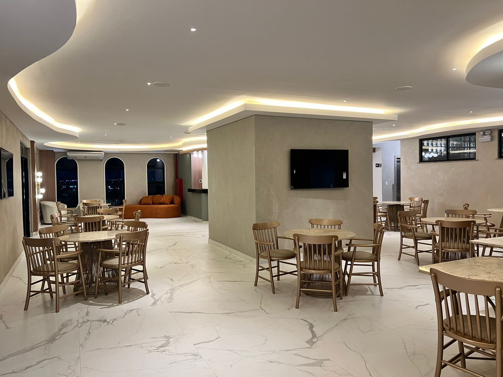 A spacious dining area with marble flooring, wooden furniture, and a flat-screen TV mounted on the wall.