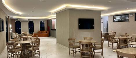 A spacious dining area with marble flooring, wooden furniture, and a flat-screen TV mounted on the wall.