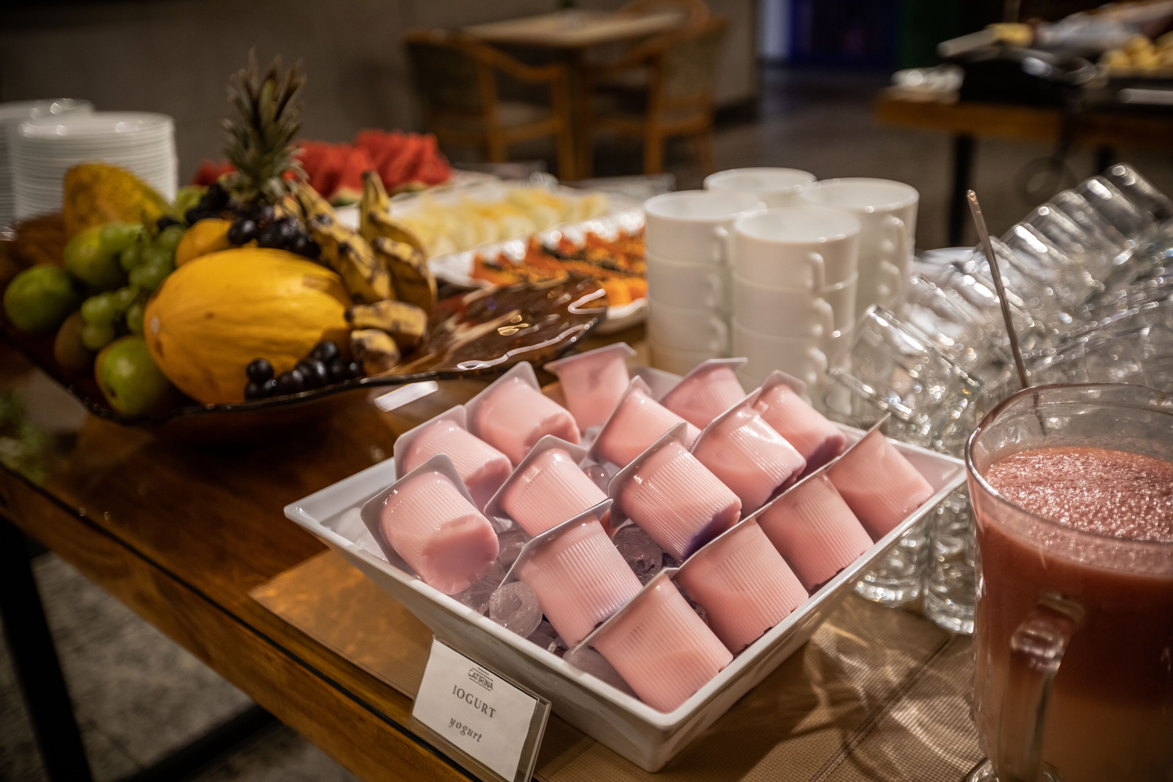 Ein Buffet mit verschiedenen Speisen, darunter Obst, eine Schale mit rosa Joghurts und ein Smoothie-Glas.