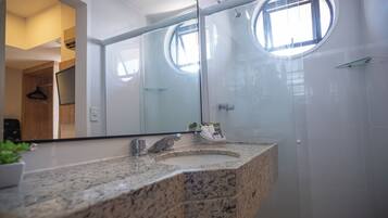 A modern bathroom with a granite countertop, a large mirror, and a glass-enclosed shower.