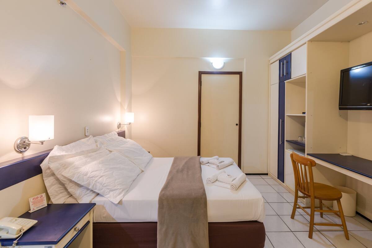 Una habitación de hotel con cama, escritorio, silla, televisor y puerta del baño.