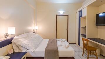 Una habitación de hotel con cama, escritorio, silla, televisor y puerta del baño.