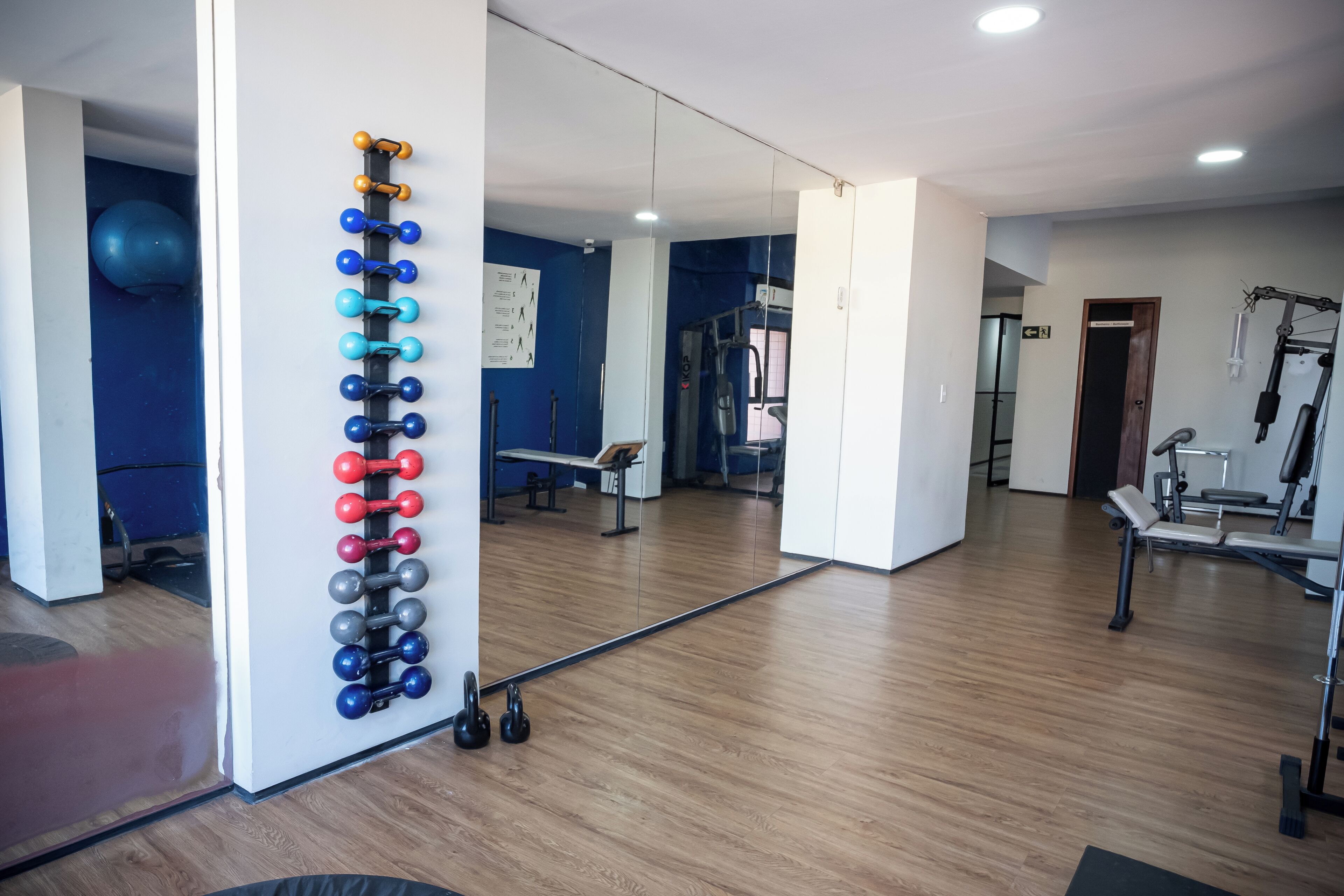 Une salle de sport équipée de matériel d’exercice, avec un miroir et un mur bleu.