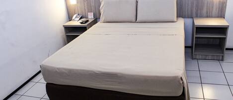 A neatly made bed with a beige cover, two bedside tables with lamps, and a wall-mounted electrical outlet.