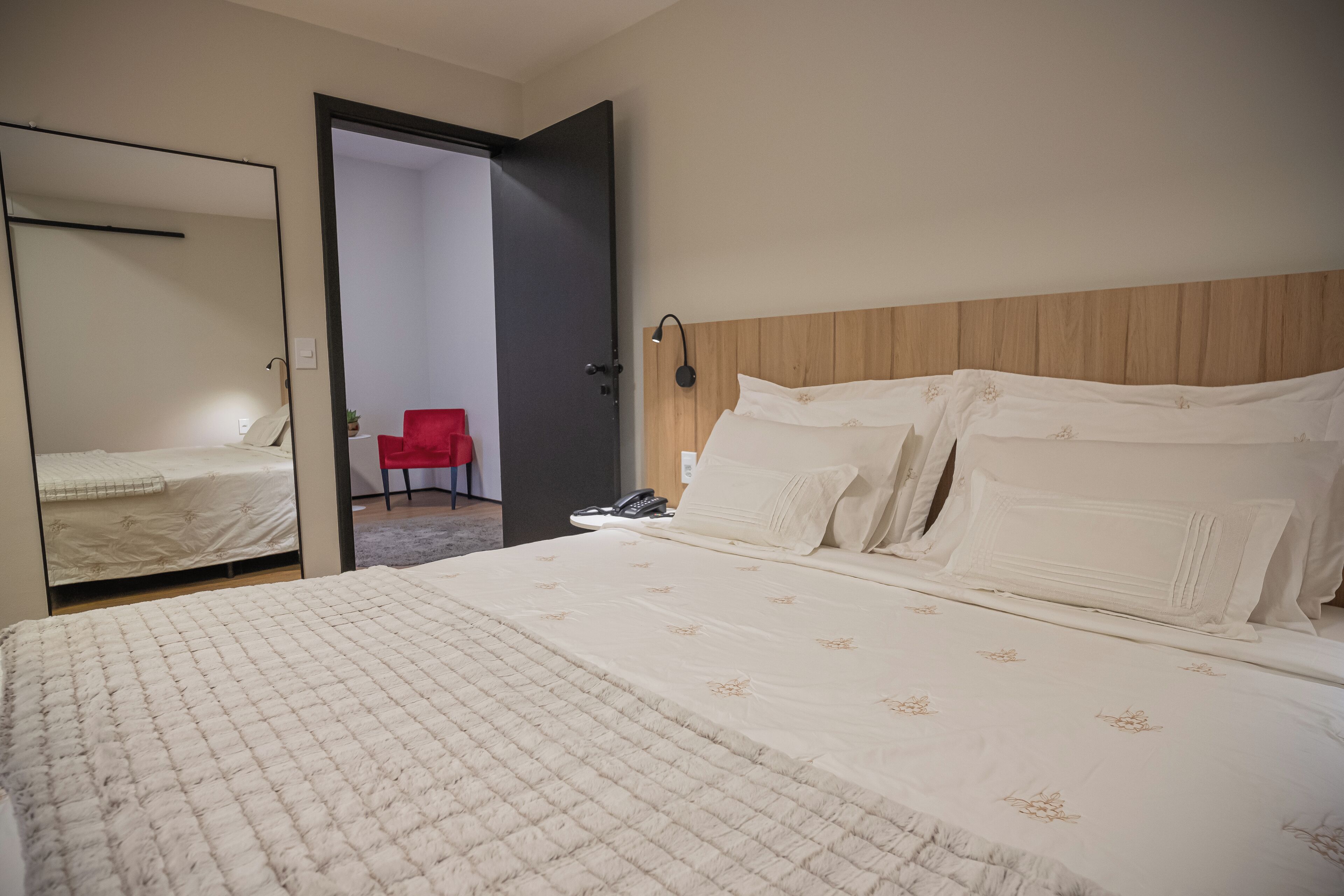 A hotel room with a large bed, a wooden headboard, a bedside table with a lamp, and a mirror.