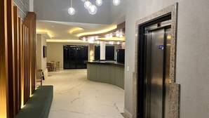 Una hall moderna con pavimento in marmo, una reception, un'area salotto e un ascensore.
