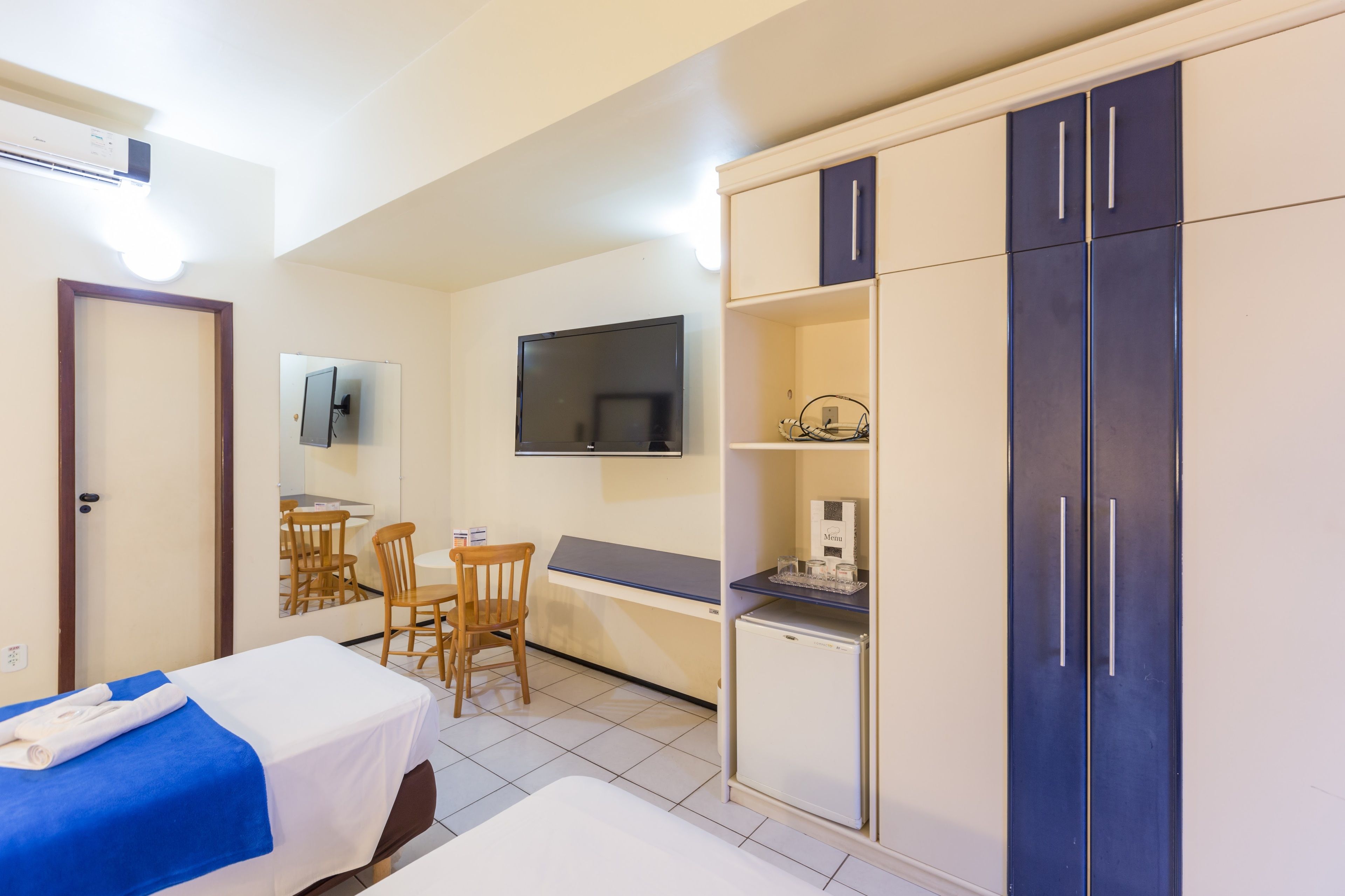 A hotel room with a bed, a desk, a chair, a TV, and a wardrobe.