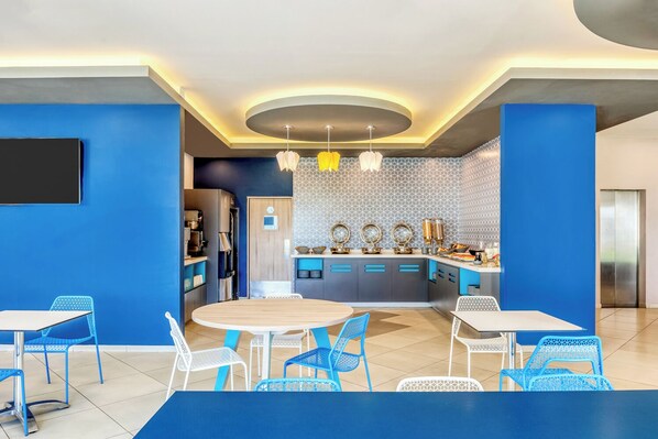 Una cocina moderna con armarios azules y grises, una isla central y una zona de comedor con sillas azules y una mesa redonda.