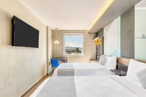 A hotel room with a bed, a desk, a chair, a TV, and a window with a view of the city.
