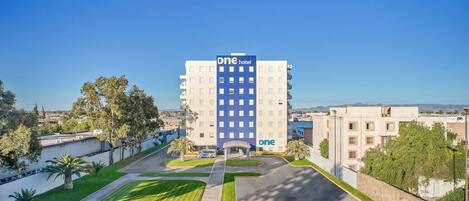 A One hotel building with a modern design, featuring a central courtyard with a fountain and surrounding greenery.