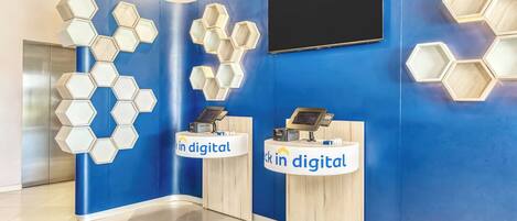 Un área de recepción con paredes azules, lámparas hexagonales y dos mostradores con la etiqueta 'En digital'.