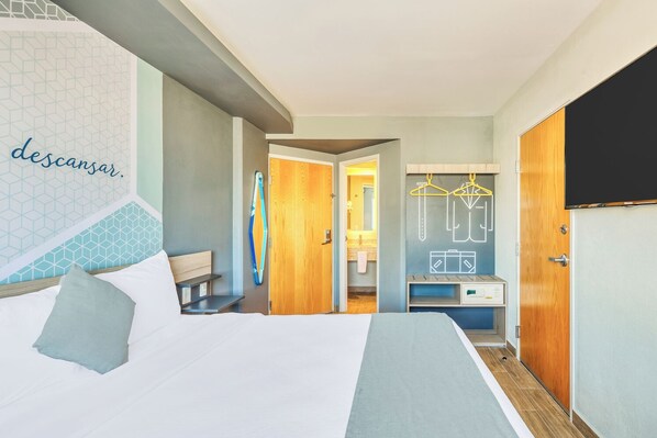 Habitación de hotel con cama, escritorio, armario y baño visible a través de una puerta abierta.