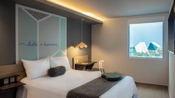 Una habitación de hotel moderna con cama, mesita de noche, lámpara y ventana con vista a la ciudad.