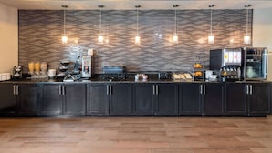 Une cuisine moderne avec des meubles de couleur sombre, un pare-feu en carreaux, des luminaires suspendus et un coin café.