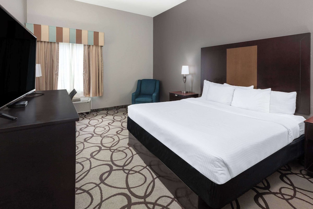 Ein Hotelzimmer mit einem großen Bett, einem Schreibtisch mit Computer, einem Stuhl und einer Lampe.